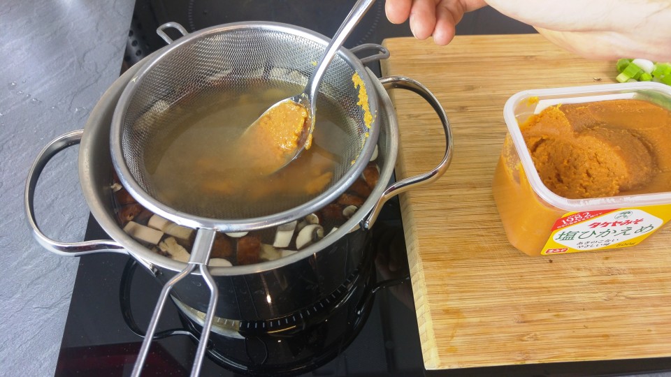 Miso Paste mit Hilfe eines Siebs in der Suppe verrühren